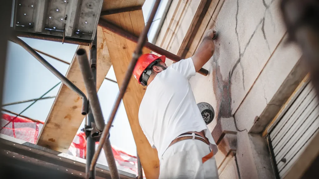 Operaio in piedi su un'impalcatura che esegue lavori di restauro della facciata di un vecchio edificio per la rigenerazione urbana