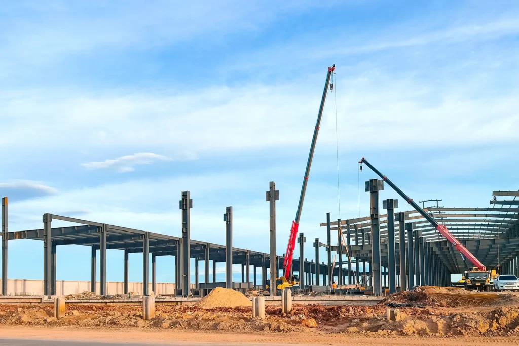 Costruzione di capannone industriale con operai e gru che installano copertura metallica su struttura portante